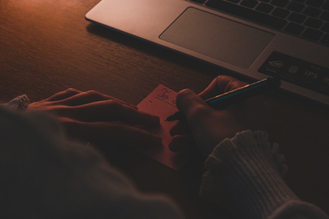 Close-up of hands typing on a laptop keyboard with notes nearby